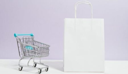 Minimalist image of a white shopping bag and mini cart on a soft pastel background.